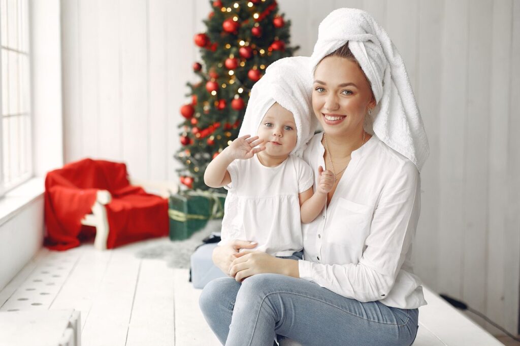 Happy mother and daughter in matching towels and white tops by Christmas tree.