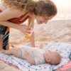 A joyful mother enjoys a sunny day at the beach interacting with her baby, creating warm family memories.