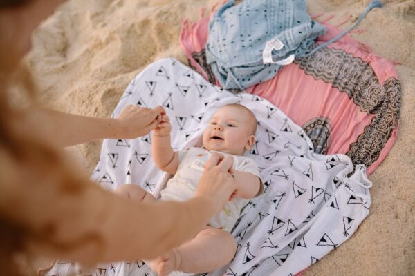 A joyful baby on the beach with parent, enjoying playtime on a sunny day.