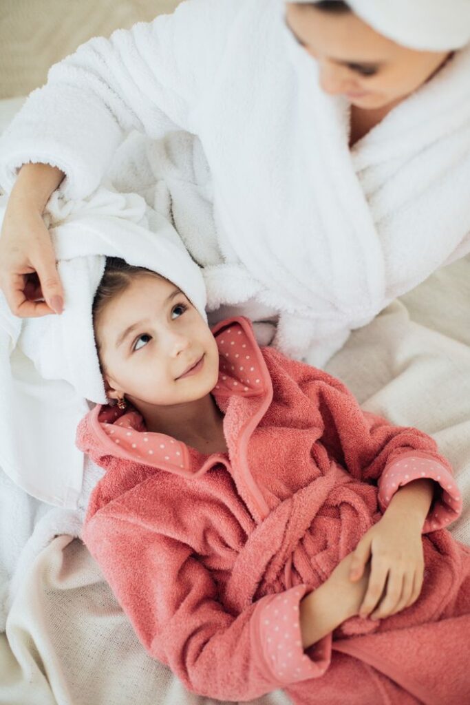 Mother and daughter in bathrobes sharing a relaxing moment indoors, epitomizing comfort and togetherness.