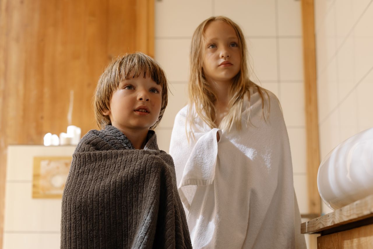 Two children wrapped in towels after a bath, enjoying the warmth indoors.