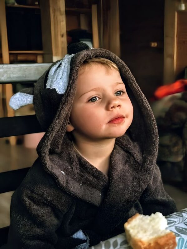 Adorable child in a cozy hooded robe, enjoying a meal at home.