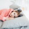 pexels-photo-6202206-6202206 A young girl in a cozy pink robe lying comfortably on a bed with soft pillows.