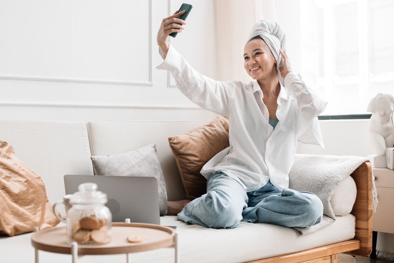 Woman sitting on a sofa, taking a selfie on a smartphone in a cozy living room.