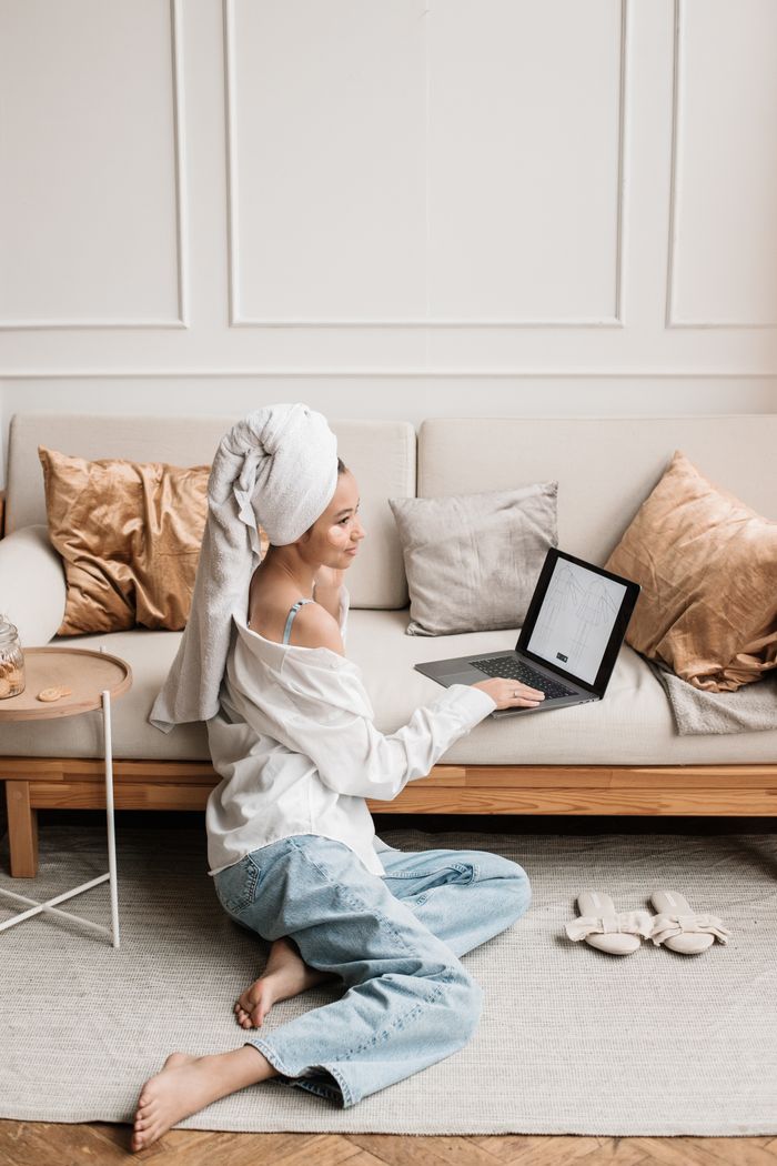 Young woman sitting on floor with laptop, wrapped in a towel indoors.