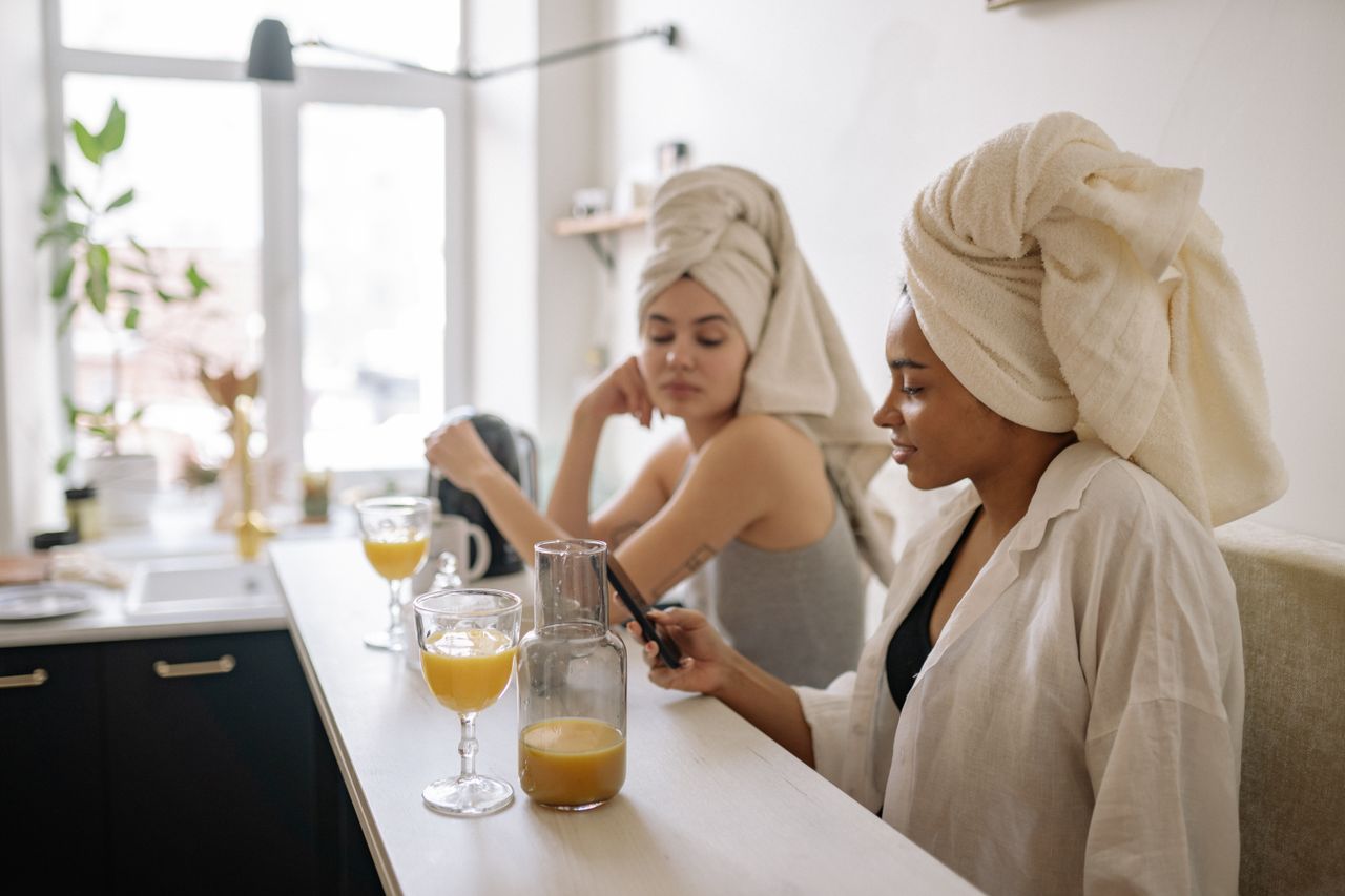 Two women enjoying a cozy morning with orange juice and phones in a bright kitchen.