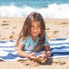 A joyful child lying on a beach towel by the shore, enjoying summer sand.